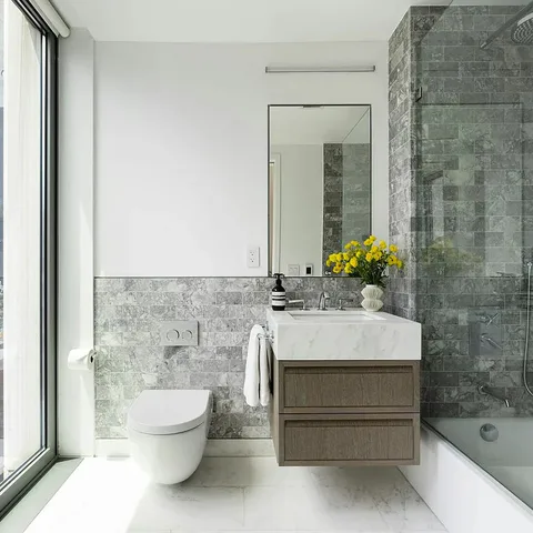 Secondary bathroom with a floating vanity, stone tile and a corner window at Midtown Luxury Residences, 30 East 31 Street, New York City, interior design by Alexandra Peck Design