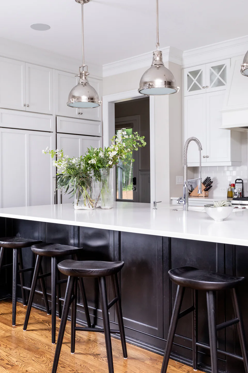 Kitchen island with white countertop, fresh greenery and black-painted base with counter stools, integrated white cabinetry beyond at Durham Transitional, Durham, North Carolina, interior design by Alexandra Peck Design