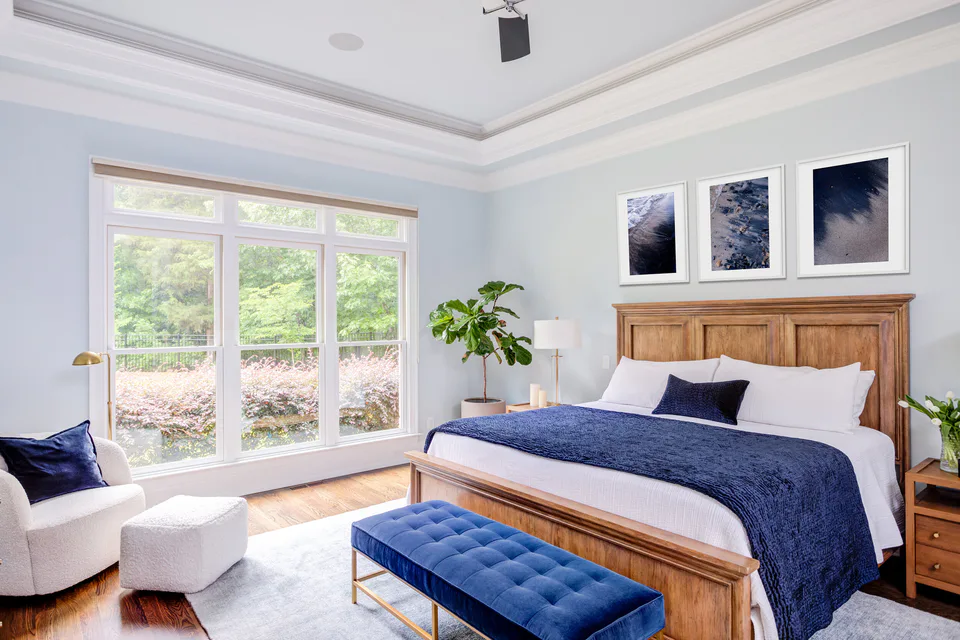 Main bedroom with a wood bed, deep blue velvet throw and tufted velvet bench, a boucle swivel chair and three framed prints at Durham Transitional, Durham, North Carolina, interior design by Alexandra Peck Design