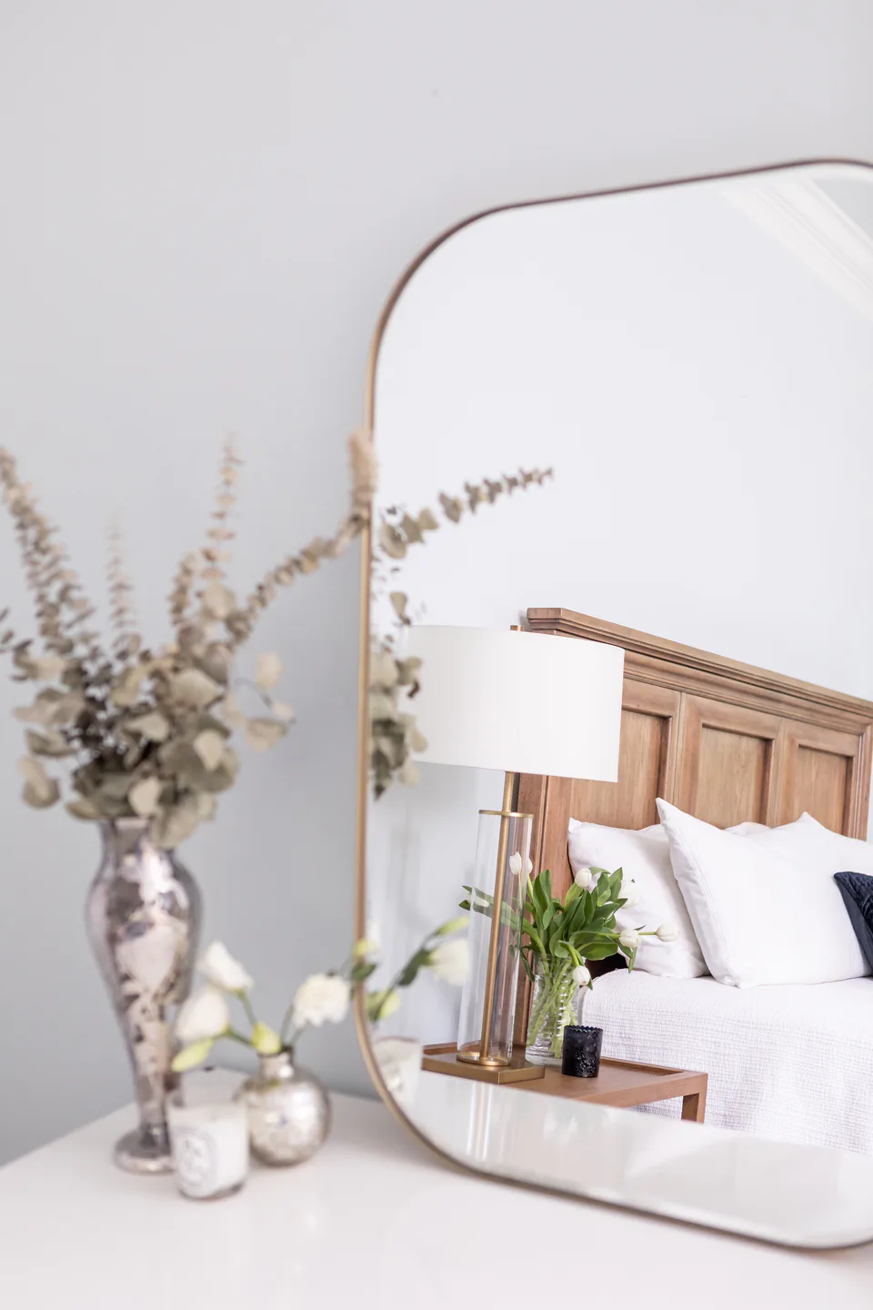 Nickel vases with dried stems on the vanity beside a large brass-framed mirror in the main bedroom at Durham Transitional, Durham, North Carolina, interior design by Alexandra Peck Design