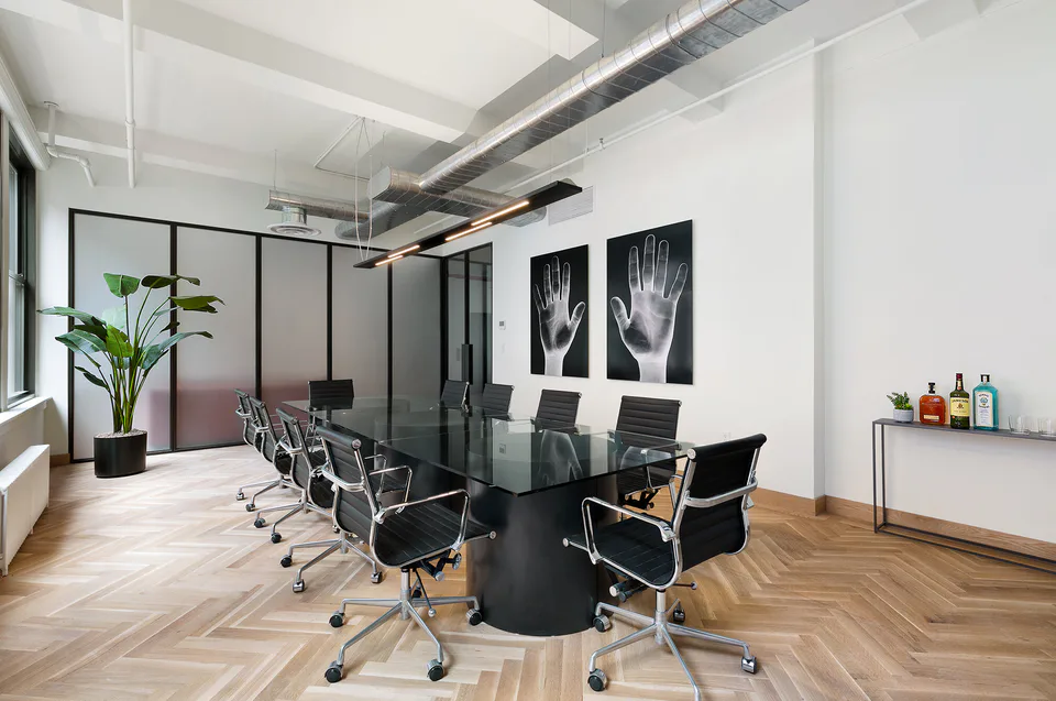 Conference room with a black glass table, black leather task chairs, a linear pendant and two framed hand photographs beside a glass partition at Flatiron Workplace, 3 East 28th Street, New York City, interior design by Alexandra Peck Design