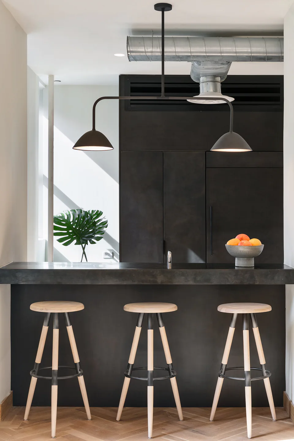 Pantry bar with blackened steel cabinetry, aged zinc counter, three wood and steel stools and black pendants at Flatiron Workplace, 3 East 28th Street, New York City, interior design by Alexandra Peck Design