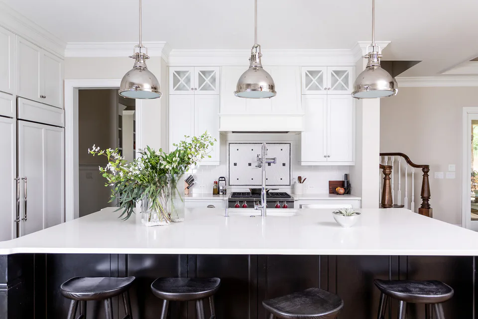 White kitchen with polished chrome pendants, a black-painted island and dark wood counter stools at Durham Transitional, Durham, North Carolina, interior design by Alexandra Peck Design