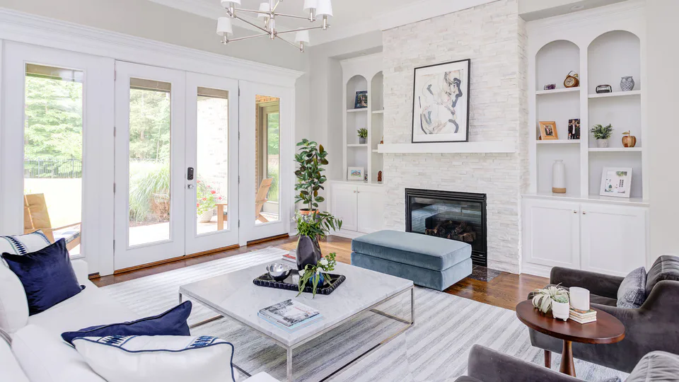 Living room with a white linen sofa, navy pillows, a marble coffee table and a white stone fireplace at Durham Transitional, Durham, North Carolina, interior design by Alexandra Peck Design