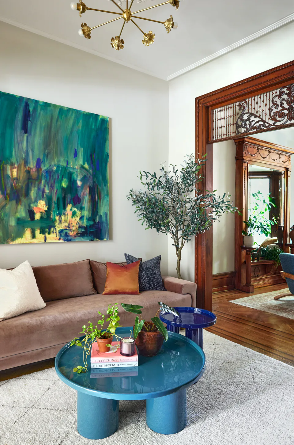 Cocktail lounge with a velvet sofa, enameled teal nesting coffee table and a vibrant original artwork beneath a vintage brass chandelier at the Prospect Heights Brownstone, Brooklyn, New York, interior design by Alexandra Peck Design