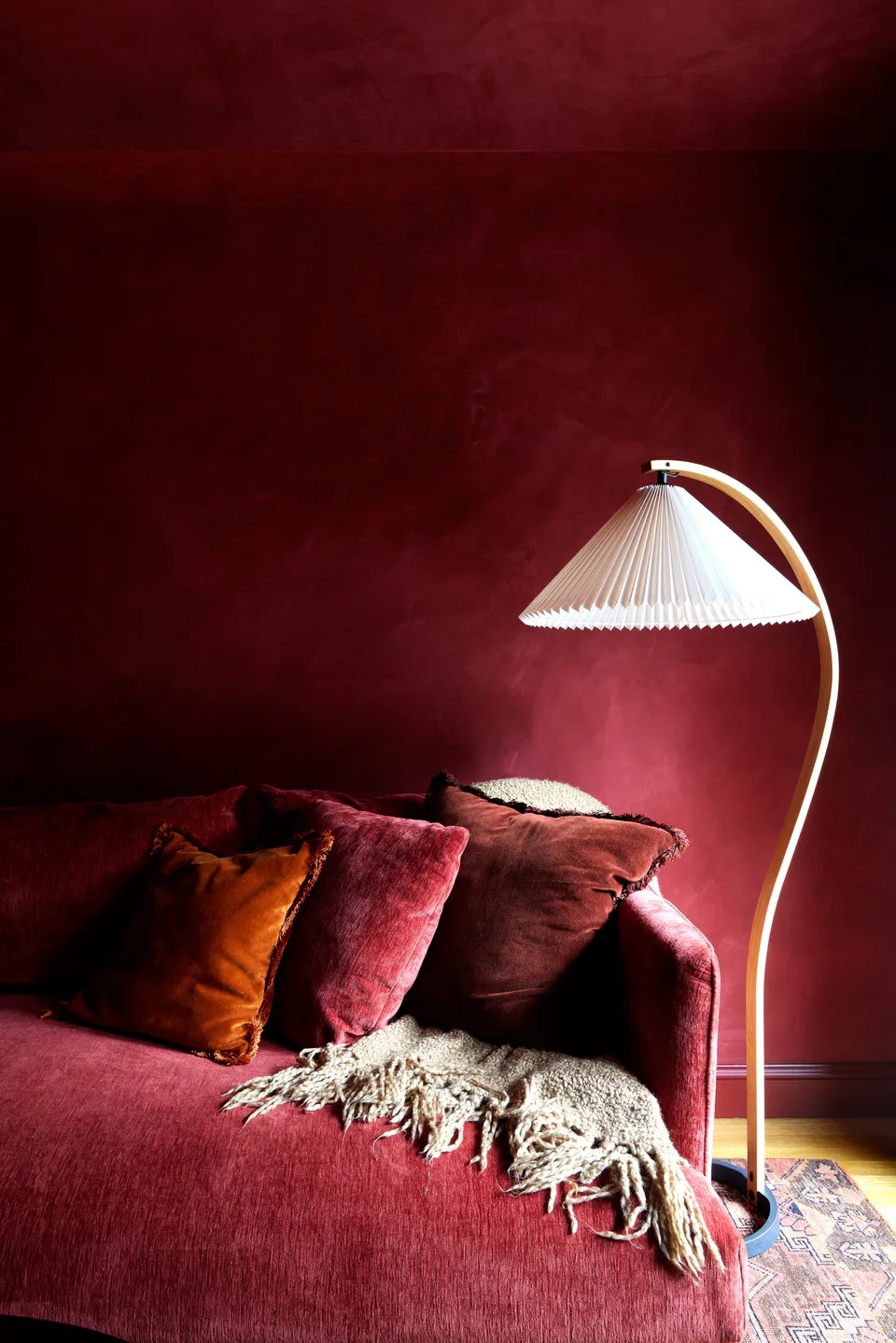 Burgundy chenille sofa with color-coordinated pillows, a throw and a vintage mid-century floor lamp against the burgundy plaster in the library at the Prospect Heights Brownstone, Brooklyn, New York, interior design by Alexandra Peck Design