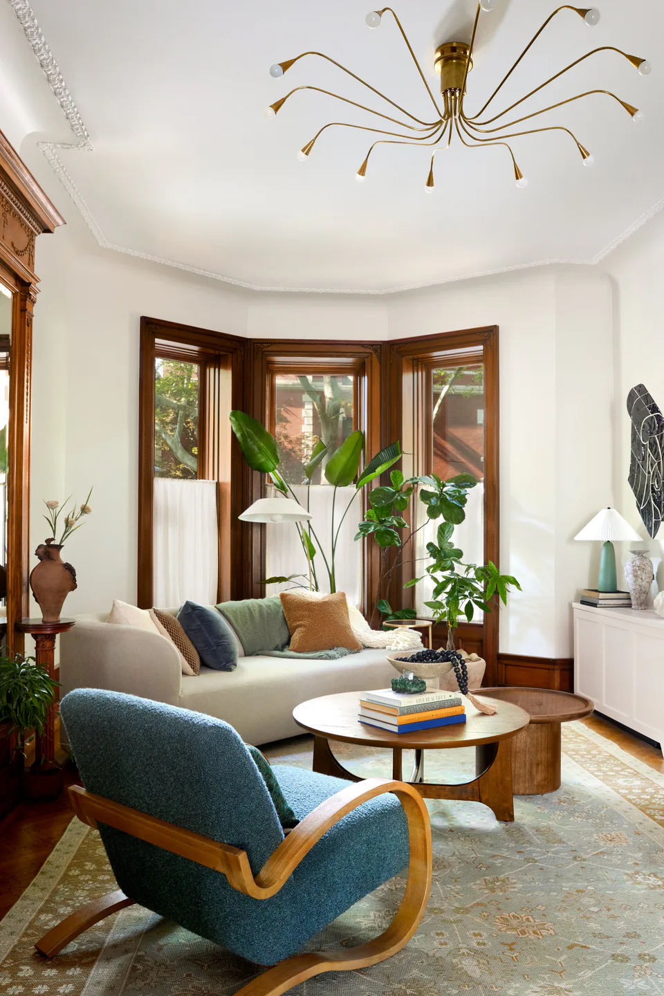 Parlor living room with a curved sofa and blue armchair before the oversized bay windows at the Prospect Heights Brownstone, Brooklyn, New York, interior design by Alexandra Peck Design