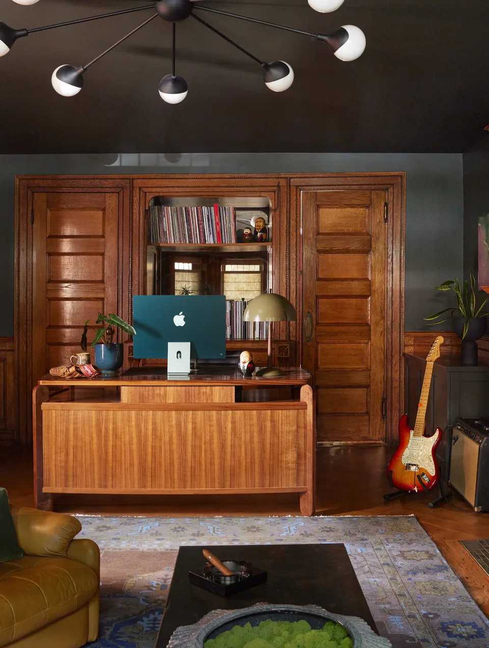 Walnut desk before the original wood built-ins and record shelves, under a sputnik chandelier, in the moss-green study at the Prospect Heights Brownstone, Brooklyn, New York, interior design by Alexandra Peck Design