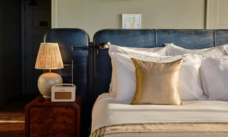 Large bedroom with a blue leather headboard, a pleated table lamp and a burl bedside chest at Soho House Nashville, Nashville, Tennessee, interior design by Alexandra Peck Design