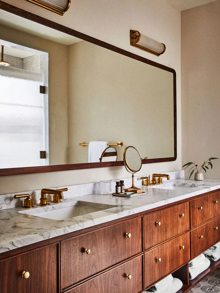 Bathroom with a walnut double vanity, a marble countertop and unlacquered brass fixtures at The Pinch Hotel, Charleston, South Carolina, interior design by Alexandra Peck Design