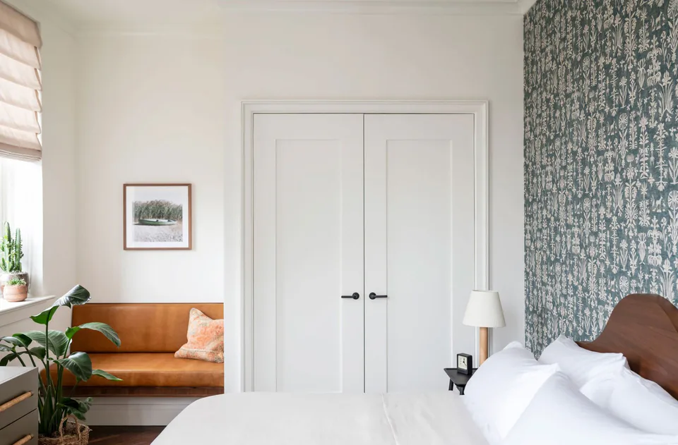 Guest bedroom with patterned wallpaper, white double doors and a leather sofa beneath the window at The Pinch Hotel, Charleston, South Carolina, interior design by Alexandra Peck Design