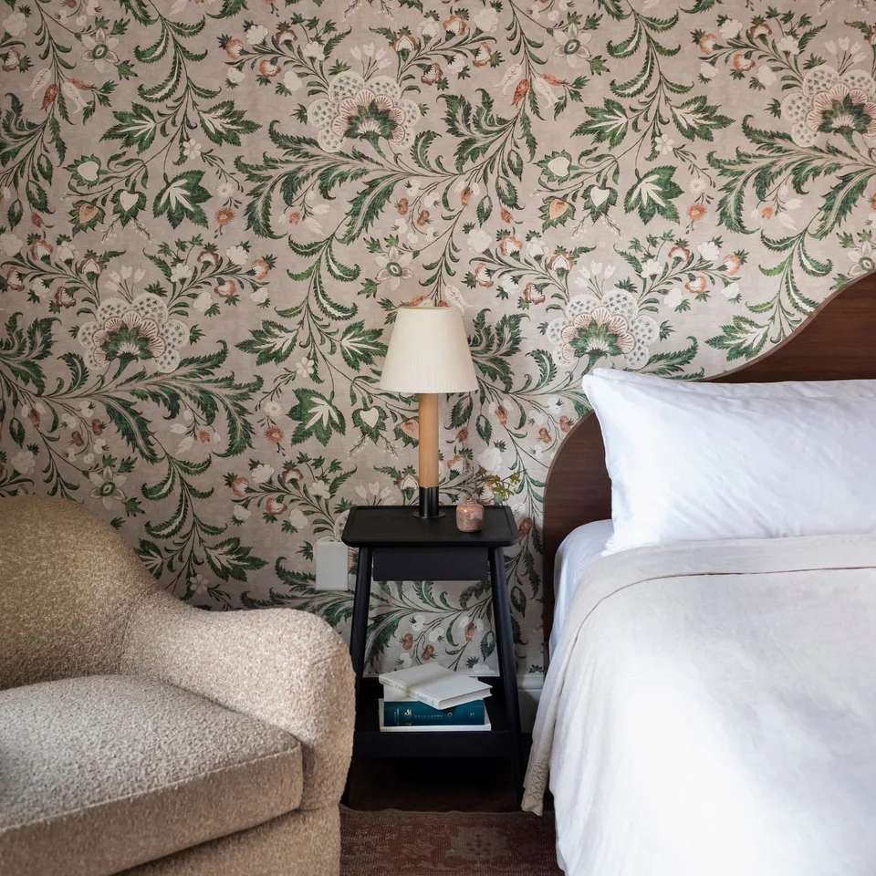 Bedroom with a floral wallpaper, a curved bouclé chair and a black bedside table at The Pinch Hotel, Charleston, South Carolina, interior design by Alexandra Peck Design