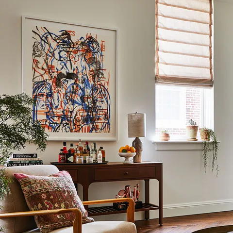 Detail: colorful abstract painting above a wooden console and an armchair with a printed cushion in a living room at The Pinch Hotel, Charleston, South Carolina, interior design by Alexandra Peck Design