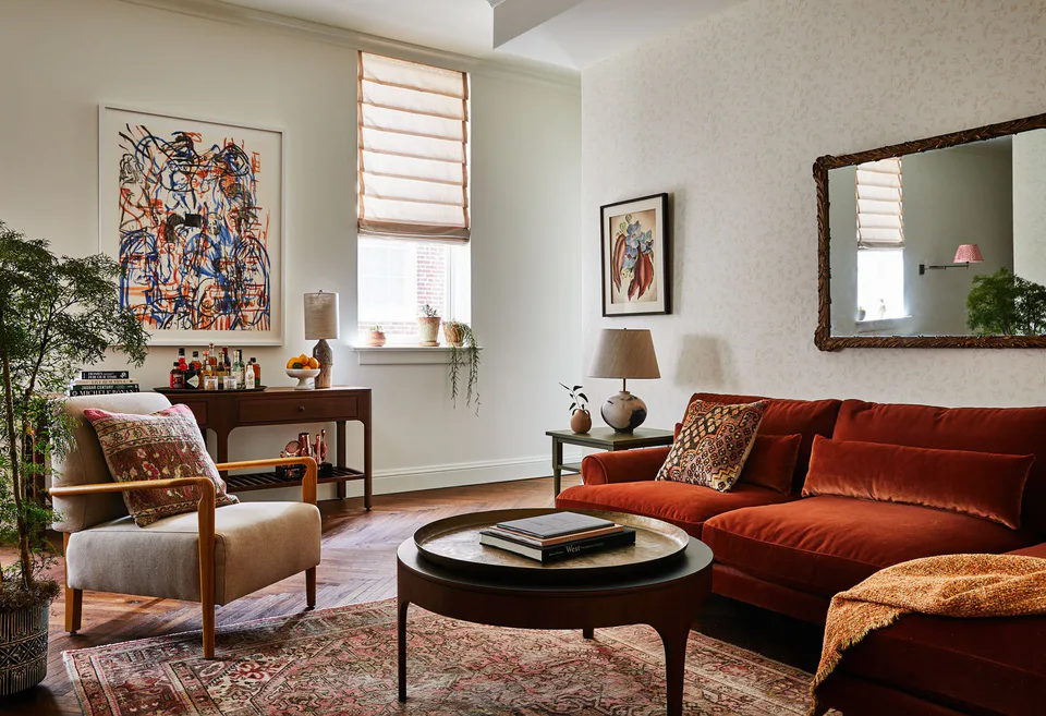 Living room with a rust velvet sofa, a round coffee table, an armchair and a colorful painting at The Pinch Hotel, Charleston, South Carolina, interior design by Alexandra Peck Design