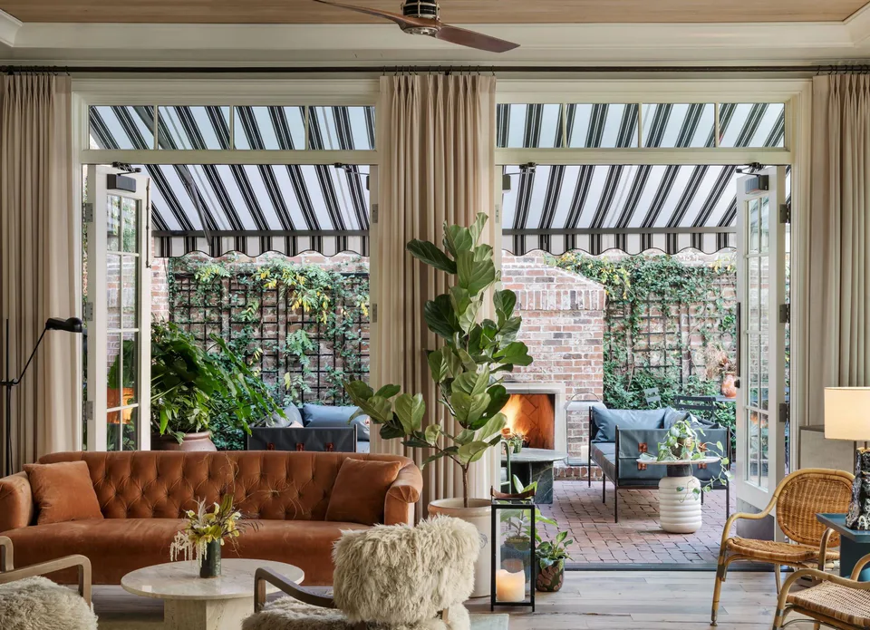 Hotel lobby with a tufted terracotta sofa and shearling chairs, its doors open to the garden courtyard under striped awnings, at The Pinch Hotel, Charleston, South Carolina, interior design by Alexandra Peck Design